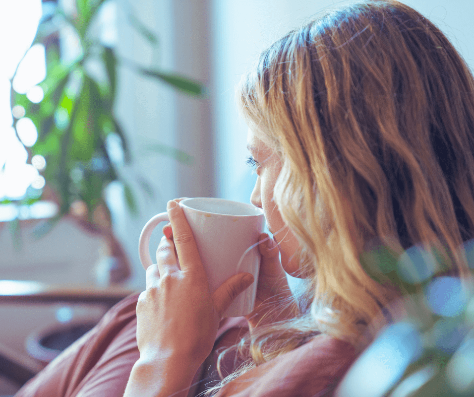How to Change Your Mindset. Blonde woman sitting in front of a window covered up...sipping her coffee looking out the window