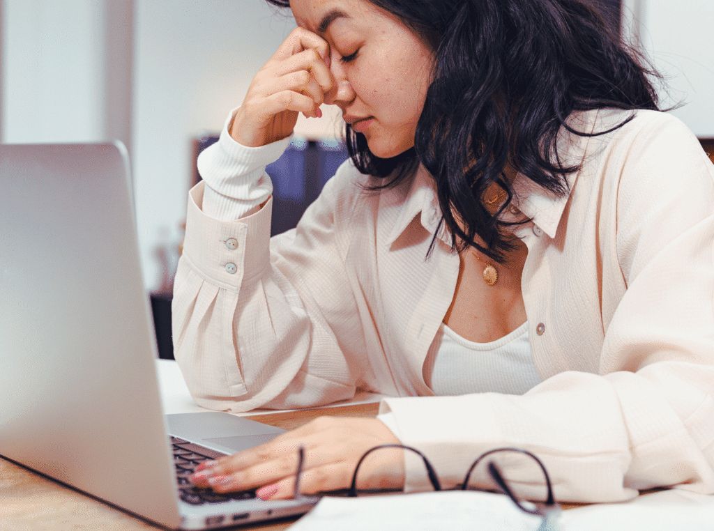 How to post on Pinterest? woman sitting at her laptop with her glasses off and her head in her hand looking frustrated.