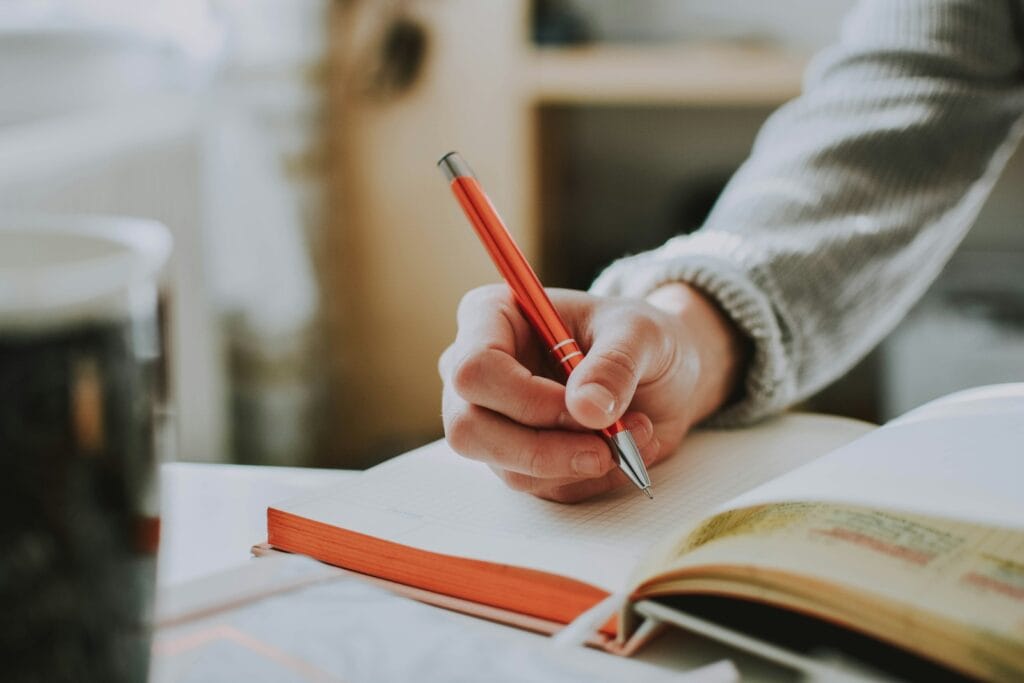 What should I write about? person holding on red pen while writing on book
