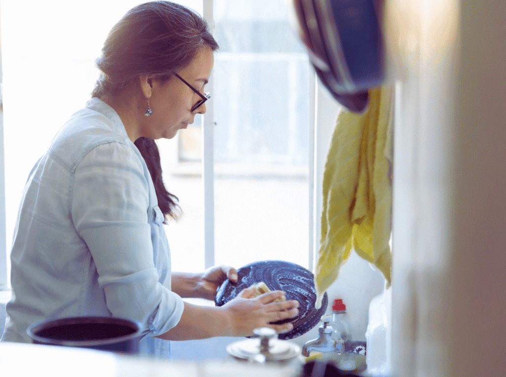 the magic of ordinary days. woman with glasses washing dishes at the sink.