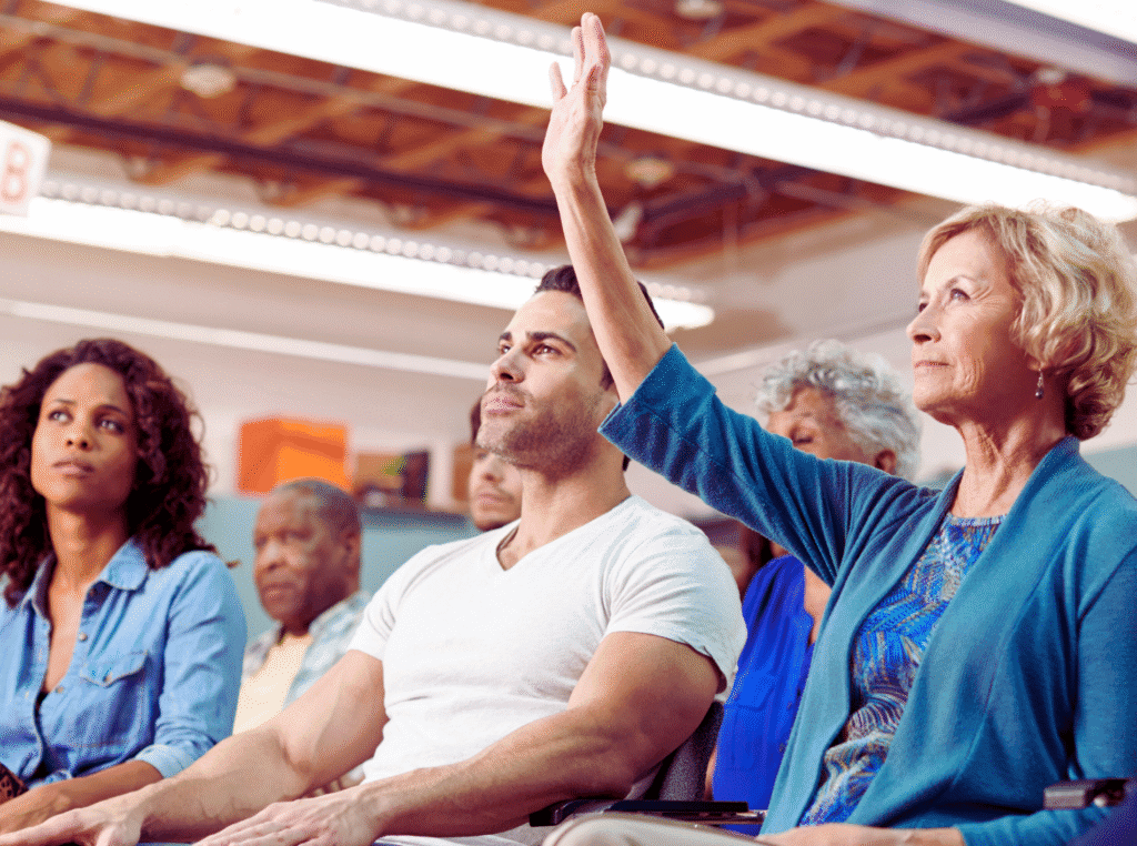 Who owns Pinterest? image of a room full of people African woman, caucasion male and caucasion older woman with her hand up to ask a question.