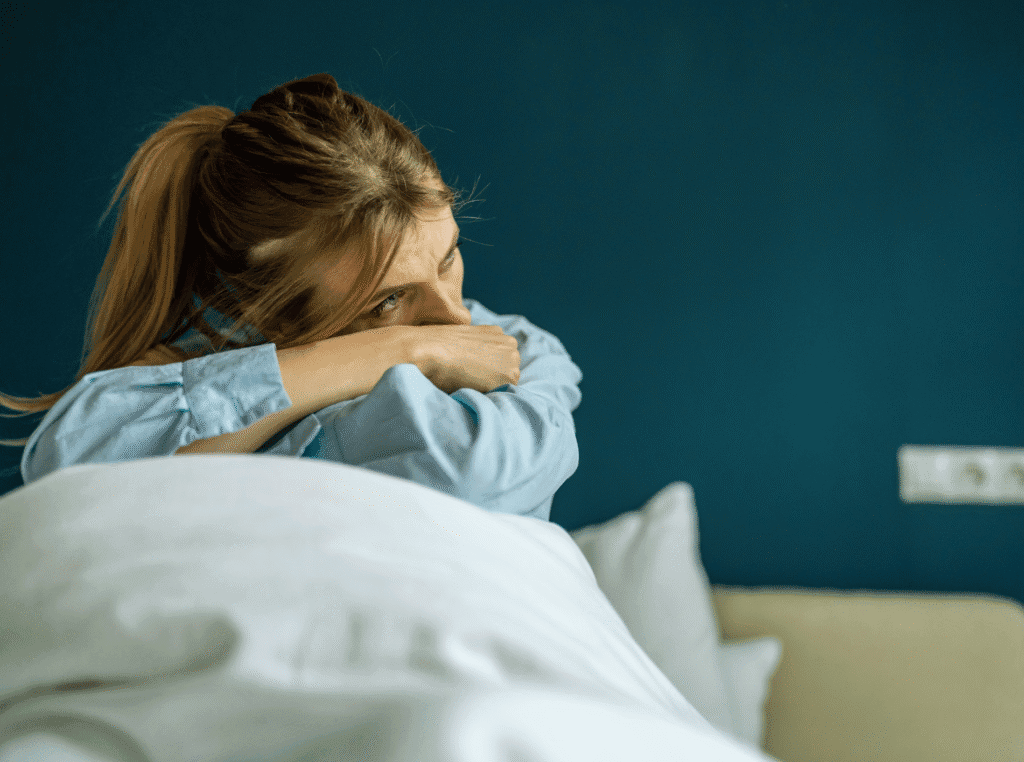 Live Life Without Regrets. woman sitting up in bed with her head laying in her arms, unhappy.