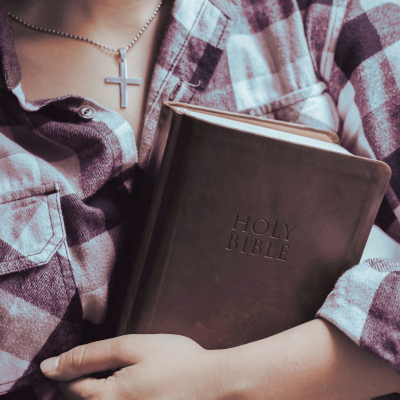 Bible verses about forgiveness. woman wearing a cross is holding a bible close to her chest.
