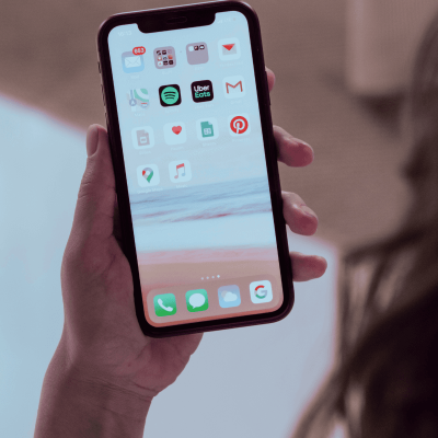 How to post on Pinterest? theres a person's hand holding their cell phone and on the screen are different apps, including Pinterest.