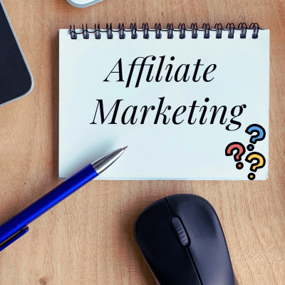 How Does Affiliate Marketing Work. spiral notebook on desk open with the wors affiliate marketing, then 3 question marks at the end. a computer mouse and a pen next to it.