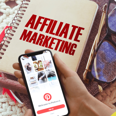 How to use pinterest for affiliate marketing. notebook on the table with the words affiliate marketing on the cover, a pair of sunglasss to the right of it and a woman's hands above it holding a smart phone with Pinterest opened on the screen. Pairing affiliate marketing and pinterest together.
