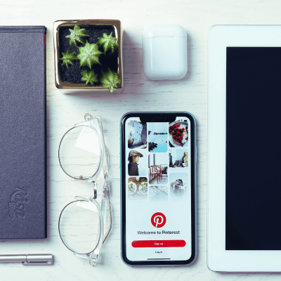 Pinterest board name ideas. image of a smart phone with pinterest on the screen sitting on a desk with glasses next to it and a few other items.