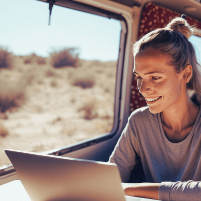 How to create digital products. woman sitting at her laptop smiling and working whle she's inside an rv in the middle of the country.