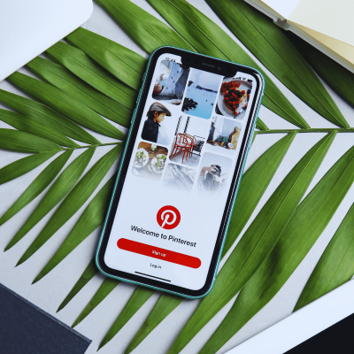 How to make money on pinterest, theres a smartphone open to pinterest that and it's laying on green leaves.