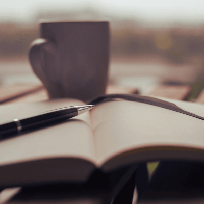 journal writing therapy. outside sits an open journal with a pen on top and a cup of coffee or tea above it.