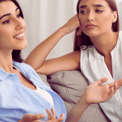 people who pretend to care. 2 women sitting together. one is talking and smiling. the other is looking bored like shes pretending to care about what is being said.